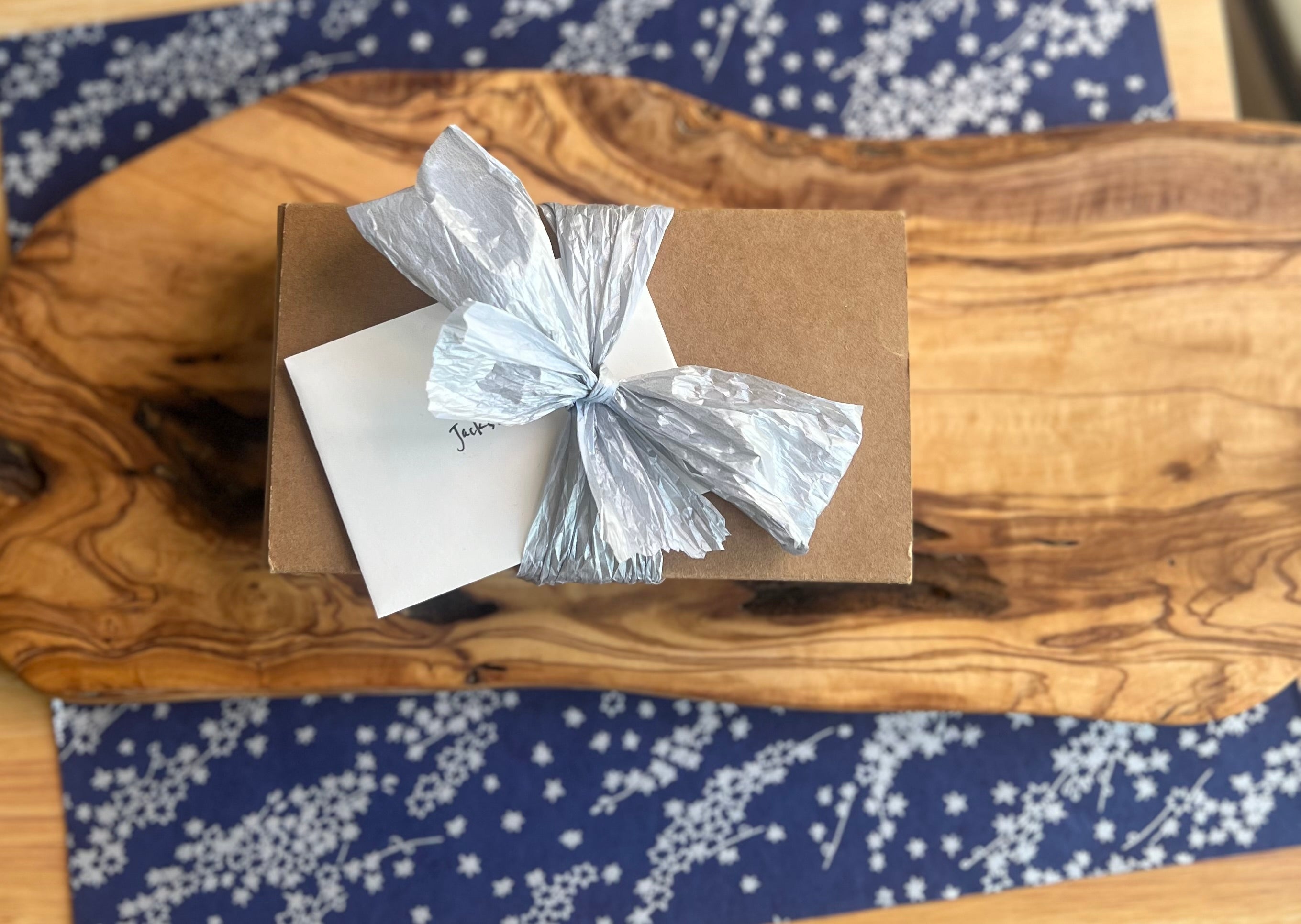 Gift box with a silver bow and a gift card on a wooden surface with a blue star patterned paper underneath